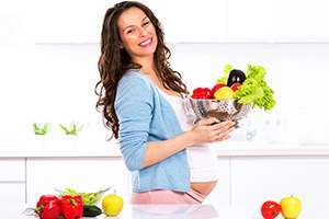 smiling pregnant woman holding fruits and vegetables in colander