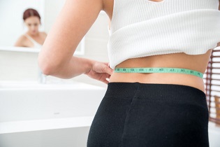 Close-up of woman measuring waist in bathroom