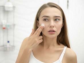 Young beautiful woman applying cream to face in the bathroom